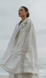 the woman in a white kimono is standing on the beach