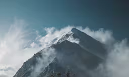 a snowy mountain with trees and clouds below