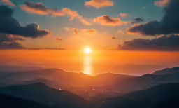 the sun setting over a mountain range with water below