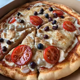 sliced and finished pizza with tomato slices, olives, and blueberries