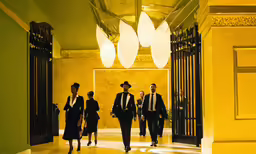 men in suits are walking down a hall towards a building