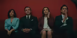 three people sit on a couch in front of a red wall