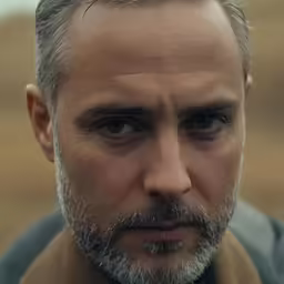 man with grey hair and beard standing in field with mountains