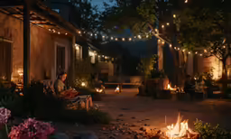 a group of people sitting in front of a building with some lights hanging over it