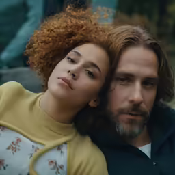 a man and woman look forward while leaning against each other