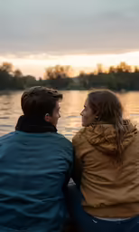 two people sitting by the water looking at each other