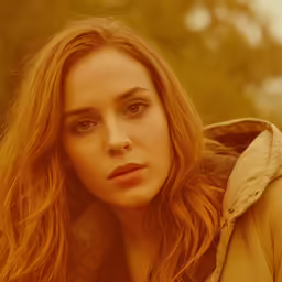 the woman is wearing a jacket and looking directly into the camera
