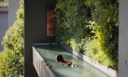 a woman lounging in a long pool that has plant life on the wall