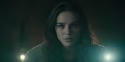 a woman looking to her left in the dark with a light shining on her face