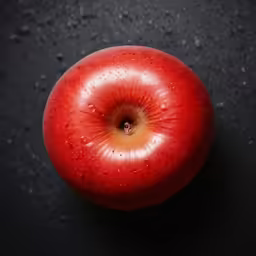an apple sits on a black surface while drops of water are covering it