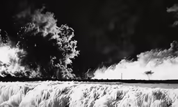 some waves are crashing under a black sky