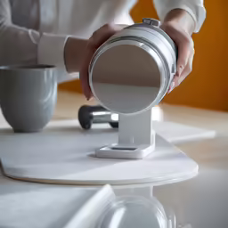 a person holding a metal camera in front of a white cup