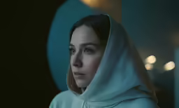 a woman standing in a dark room wearing a hood