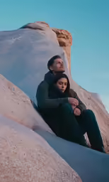a man and woman are sitting on top of a large rock