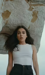 a woman is holding on to a rock and looking up
