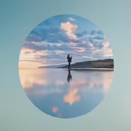 a lone person stands by the water with his arms behind him as he looks towards the sunset