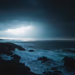 the ocean at night with some dark clouds and rocks
