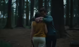 two people walking in the woods near many trees