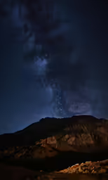 the night sky has some stars above some mountains