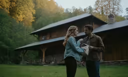 two people are standing in front of a log house