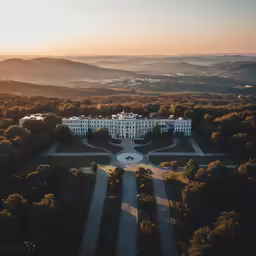 a very large building surrounded by trees in front of mountains
