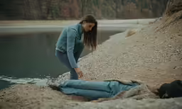 two people are laying in the sand near water