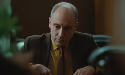 a man in a suit looks down and listens to something
