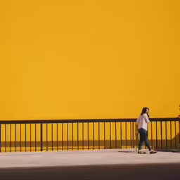 two women walking on a yellow wall with fenced area