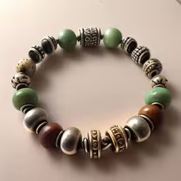the bracelet has many different beads on it,the beaded bracelet is sitting on top of a table