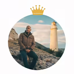 a man in a crown sitting on rocks near a lighthouse