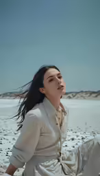 a woman sitting in the sand with her hair flowing