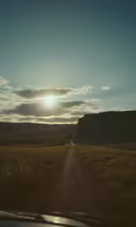 a vehicle is going on the dirt road in the distance with the sun going down