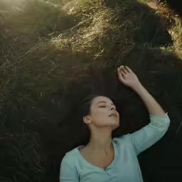 a beautiful woman laying on top of a lush green field