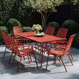 an outdoor dining area with a table, orange chairs and a black fence