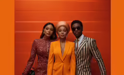 three people posing for the camera in a group against an orange wall
