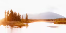 a lake surrounded by trees and mountains under a hazy sky