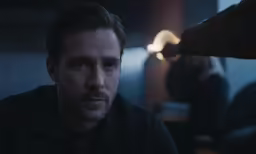 a man in a dark room with two other men looking around