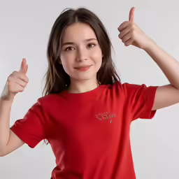 little girl in red shirt pointing at camera with thumbs up