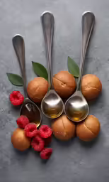 a table with silver spoons, raspberries and an oval shaped cookie
