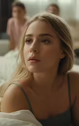 a blonde haired woman in a gray tank top sits on a bed with two other women