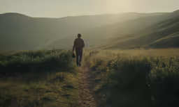 a man that is walking on the grass with some mountains in the background