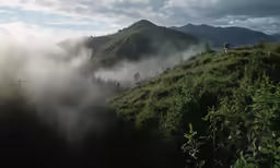a person is standing on a grassy hill, with low clouds