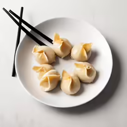 a white plate with chopsticks on it containing four dumplings