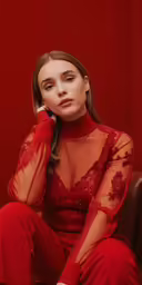 a girl sitting in front of a red wall wearing a red dress and talking on a phone