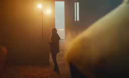 a young person walking away from a light with two light poles behind them