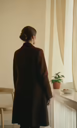 a woman standing by a window in a room with a desk and chair