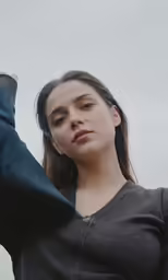 a young woman holds her hand to her ear while standing in front of the camera