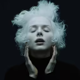 a person with white hair and makeup has her hands behind their ears