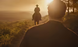 man in a cowboy hat riding his horse down a dirt path