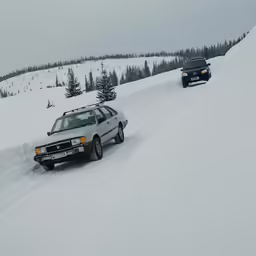 cars driving down a snow covered road on the ski slope